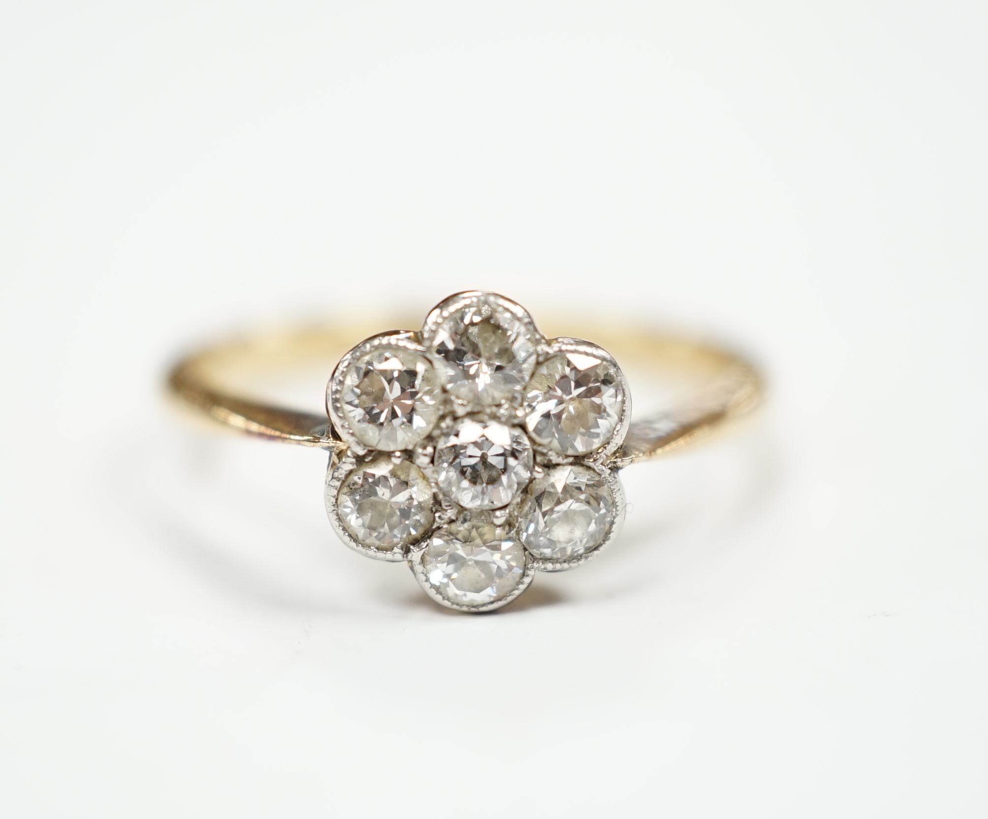 An 18ct and seven stone diamond set flower head cluster ring, size M/N, gross weight 2.9 grams.